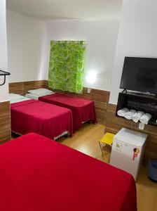 a room with two red beds and a flat screen tv at Pousada Bonita , Piranhas AL in Piranhas