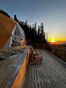 un banco en una terraza de madera con la puesta de sol en el fondo en Forbord Dome 