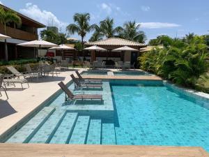 a swimming pool with chairs and umbrellas in a resort at Loft de praia - Itacimirim BAHIA in Itacimirim