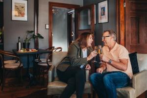 Ein Mann und eine Frau, die auf einem Stuhl sitzen und Wein trinken. in der Unterkunft William Arnott Boutique Accommodation in Morpeth