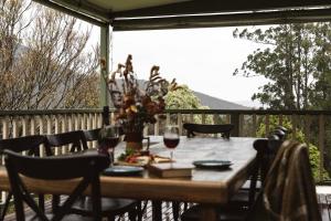 a wooden table with glasses of wine on a deck at Hey Little Joe - Cosy Retreat with Mountain Views in Warburton