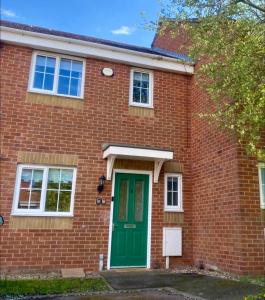 a red brick house with a green door at Oakley House - Spacious 3 Bedroom, Garden and Parking in Corby