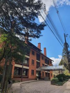 un gran edificio de ladrillo con un árbol delante de él en Duplex estilo europeu Ednamar Apartamentos Bérgamo, en Gramado