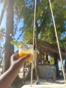 a person holding a drink in front of a shack at Paje Home in Paje