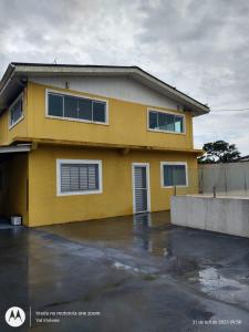 ein gelbes Haus mit einem Parkplatz davor in der Unterkunft Casa amarela cantinho de lazer in Ilha Comprida