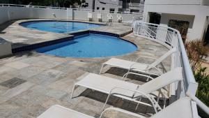 a swimming pool with white chairs next to a building at Guarujá - Praia do Tombo - Apartamento in Guarujá