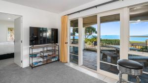 a bedroom with a television and a balcony with the ocean at Beachfront Beauty in Whangaparaoa