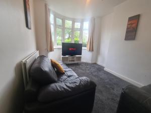 a living room with a leather couch and a television at L & J ESCAPES-4 BEDROOMs SUITABLE FOR CONTRACTORS AND FAMILIES- LARGE PRIVATE PARKING-10 MINUTES TO M6 JUNCTION 9 in Coseley