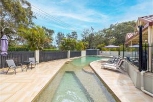 a swimming pool with chairs and a house at Nelson Bay Breeze Apartment, 29,1 Trafalgar Street - Air conditioned unit with Linen supplied, complex pool and spa in Nelson Bay