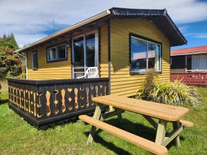 a yellow tiny house with a wooden bench in front of it at Manapouri Holiday Park in Manapouri