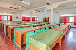 uma sala de aula com mesas de madeira e cadeiras verdes em Capital O 93236 Hotel Hapel Negara em Banyubiru