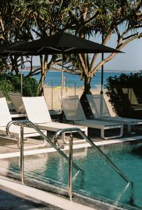 uma piscina com duas cadeiras e um guarda-sol junto a uma praia em 71 Hastings Street - Beachfront em Noosa Heads