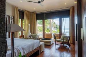 a bedroom with a bed and chairs and a large window at Eraeliya Villas & Gardens in Weligama