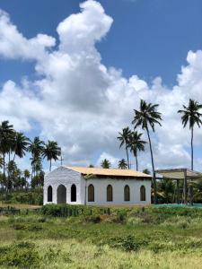 a white building with palm trees in a field at Casa Milagres do Porto - Suítes in São Miguel dos Milagres