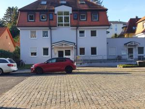 ein rotes Auto, das vor einem weißen Haus parkt in der Unterkunft Dennis Apartment in Dresden