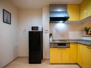 eine Küche mit gelben Schränken und einem schwarzen Kühlschrank in der Unterkunft Sumiyoshi Marie - Vacation STAY 12160 in Osaka
