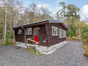 uma pequena cabana com uma porta vermelha na floresta em Bridgend Chalet on Reelig Estate Near Inverness em Kirkhill