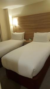 two beds in a hotel room with white sheets and pillows at Holiday Inn London Kensington High St., an IHG Hotel in London