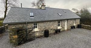 una pequeña casa de piedra con techo y 2 bancos en Newly Renovated stone cottage located 2.5 miles from Killarney Town, en Teernaboul