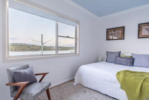 a bedroom with a bed and a window and a chair at Central Coast Jetty House in Saratoga
