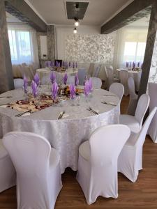 una stanza con tavolo con sedie bianche e fiori viola di Pensiunea Teo a Bilbor
