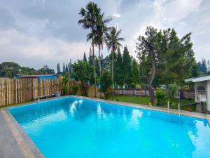 a large blue swimming pool with a fence and trees at Villa Cisarua Wulan in Brujul