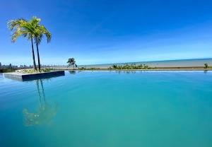 a large swimming pool next to a beach with a palm tree at UNITY Cabo Branco by PenareiaTurBr in João Pessoa