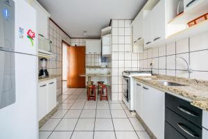 eine weiße Küche mit einer Spüle und einem Kühlschrank in der Unterkunft Amplo apto 7 min do mar na Meia Praia EIO203 in Itapema