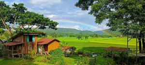 un arc-en-ciel sur un champ vert avec une maison dans l'établissement Kaewma farmstay, à Ban Khuang Kom