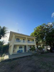 a large white house with a porch and a tree at Casa Amarela, para veraneio em Areia Dourada in Cabedelo