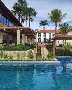 a swimming pool in front of a building with palm trees at Flat da Mata - Resort Quinta Santa Bárbara in Pirenópolis