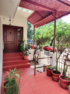 a house with a porch with potted plants and a red car at The Rustic Manor - Homestay in Bangalore