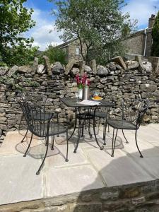 een tafel met vier stoelen en een stenen muur bij Hawksworth Cottage - Grassington Village Location in Grassington