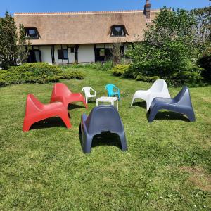 cuatro sillas de colores diferentes sentadas en el césped en Les 2 chaumières avec piscine en Épinay