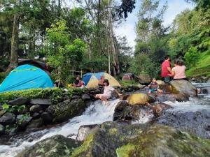 a group of people sitting in a river with tents at view cemping glamping in Bukittinggi