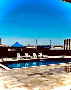 a swimming pool with chairs and tables and a blue sky at Cali Chalet in Al Karāmah