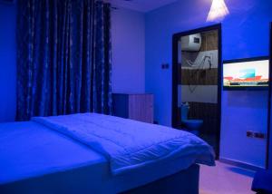 1 dormitorio azul con 1 cama y TV en Home to Home luxury apartments and suites en Benin City