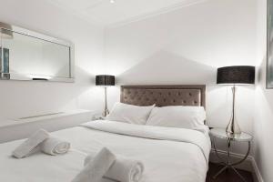 een witte slaapkamer met een groot bed met 2 lampen bij Beautiful Studio On The Strand in Londen
