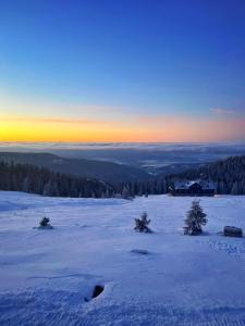 a winter sunset over a snowy field with a house in the distance at Horská bouda KUPROVKA in Strážné