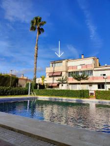 uma piscina em frente a um edifício com uma palmeira em Bungalow familiar con piscina em San Juan de Alicante