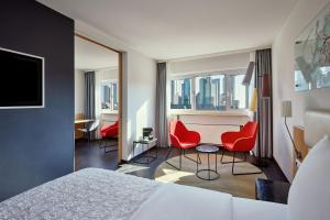 フランクフルト・アム・マインにあるル メリディアン フランクフルトのベッド1台と赤い椅子2脚が備わるホテルルームです。