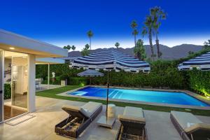 a swimming pool with umbrellas and chairs next to a house at Canyon Palms Estate- Ultra-Luxe, Pool, Spa, Firepit, Outdoor Kitchen & More in Palm Springs