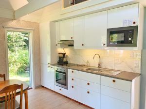 cocina con armarios blancos, fregadero y mesa en The Blomsholm Cabin en Strömstad