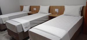 three beds in a room with white sheets at Hotel Bonina in Sao Paulo