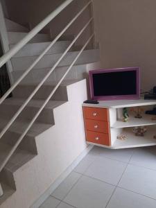 a living room with a staircase with a tv and a desk at Sobrado confortável a uma quadra do mar. in Matinhos