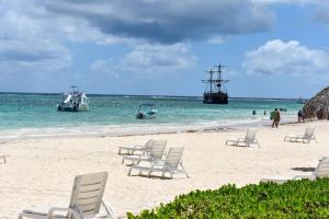 a beach with chairs and a boat in the water at Oceanfront Playa Turquesa with highspeed Wi-Fi, pools, free beach access in Punta Cana
