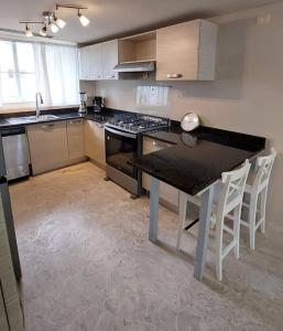 a kitchen with a black counter top and white chairs at Oceanfront Playa Turquesa with highspeed Wi-Fi, pools, free beach access in Punta Cana