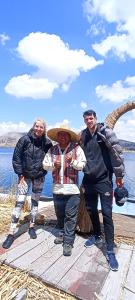 3 Personen stehen auf einem Dock in der Nähe des Wassers in der Unterkunft Uros Waliski Lodge in Puno