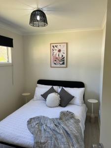 Schlafzimmer mit einem Bett mit weißer Bettwäsche und Kissen in der Unterkunft Batemans Bay North Bush Cottages in Benandarah