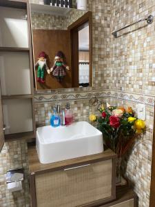 ein Badezimmer mit einem Waschbecken, einem Spiegel und Blumen in der Unterkunft Casa a 500m do Natal Luz de Gramado in Gramado